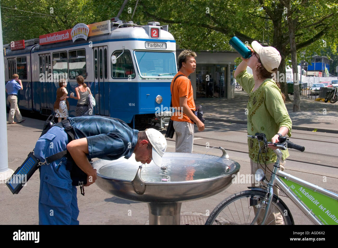 Scène de rue avec fontaine d'eau potable et rue voiture à Zurich, Suisse. L'homme à gauche est un agent d'exécution. Banque D'Images