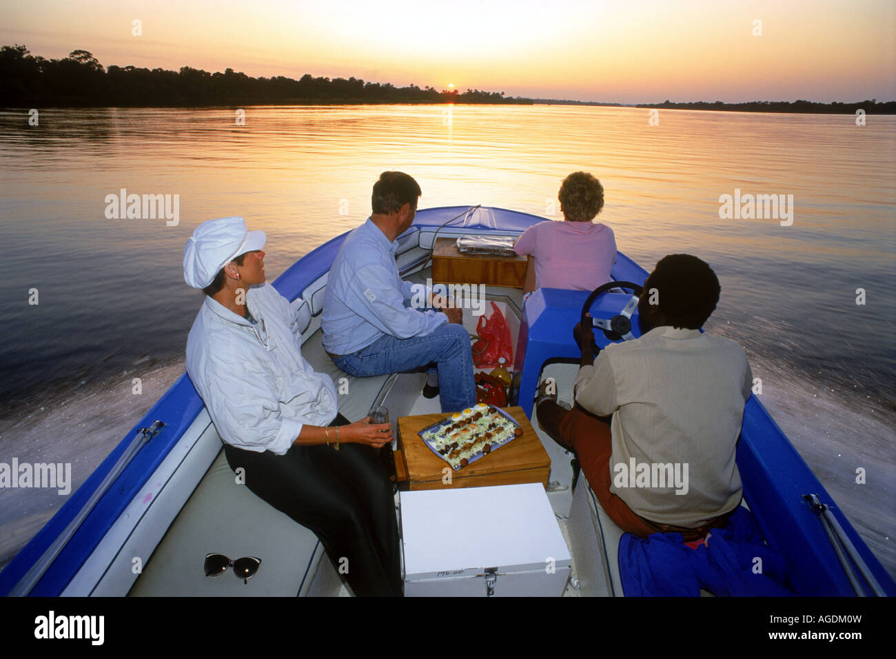 Les touristes ayant tour en bateau au coucher du soleil sur les eaux miroitantes du fleuve Zambèze entre le Zimbabwe et la Zambie Banque D'Images