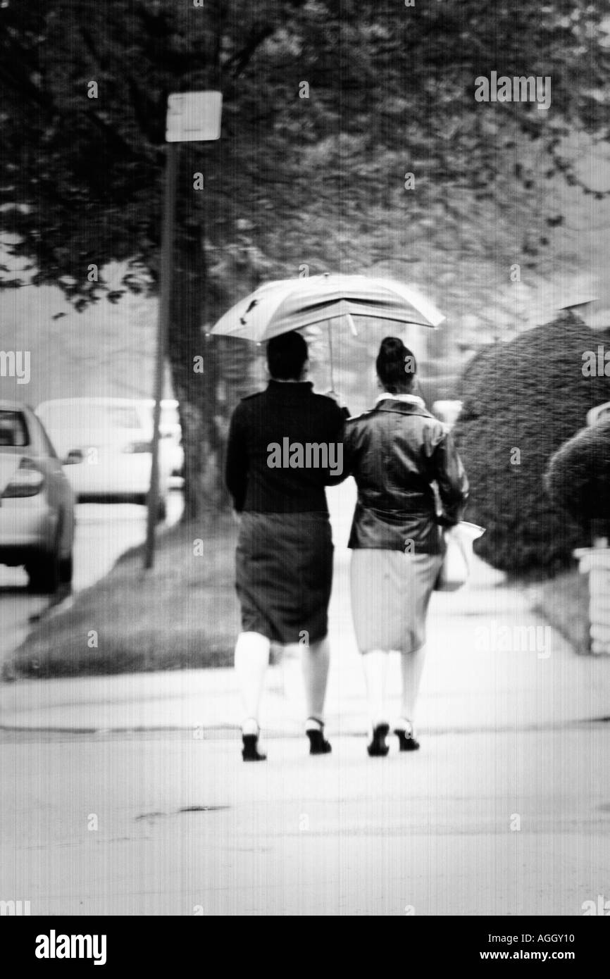 Deux femmes marchant sous la pluie, l'exécution et le partage d'un parapluie vu de derrière en jupe Banque D'Images
