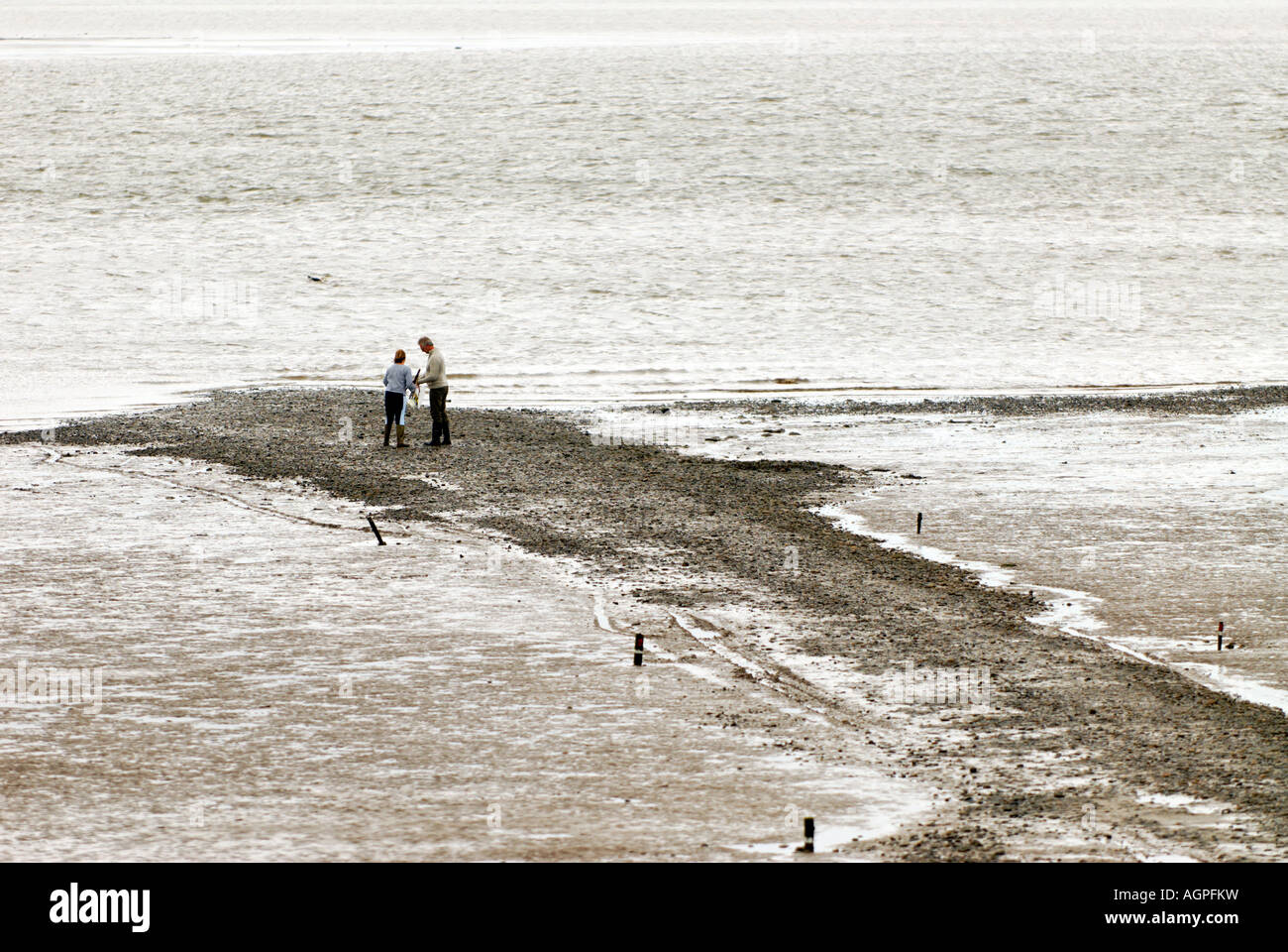 Couple de prendre une marche sur une plage de galets et de vase à marée basse Banque D'Images