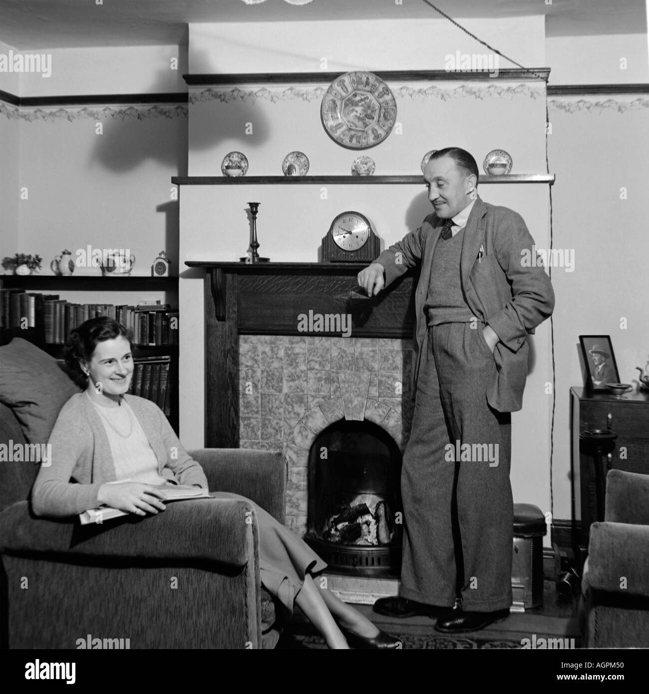 OLD VINTAGE SNAPSHOT FAMILLE PHOTOGRAPHIE DE MAN LEANING ON cheminée à la femme assise au fauteuil de lecture SALON DU LIVRE Banque D'Images