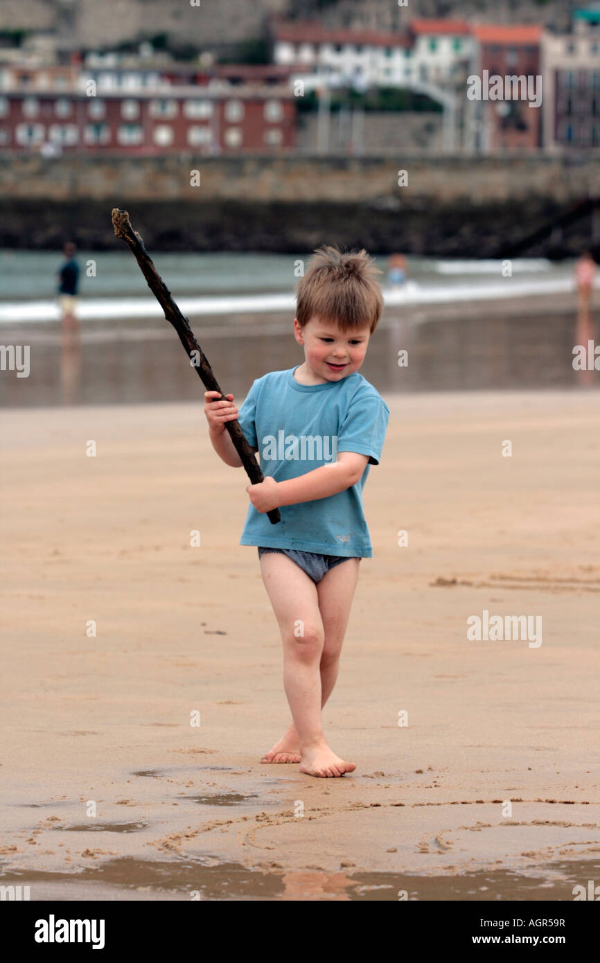 Enfant jouant sur la plage dessin dans le sable avec un bâton Banque D'Images