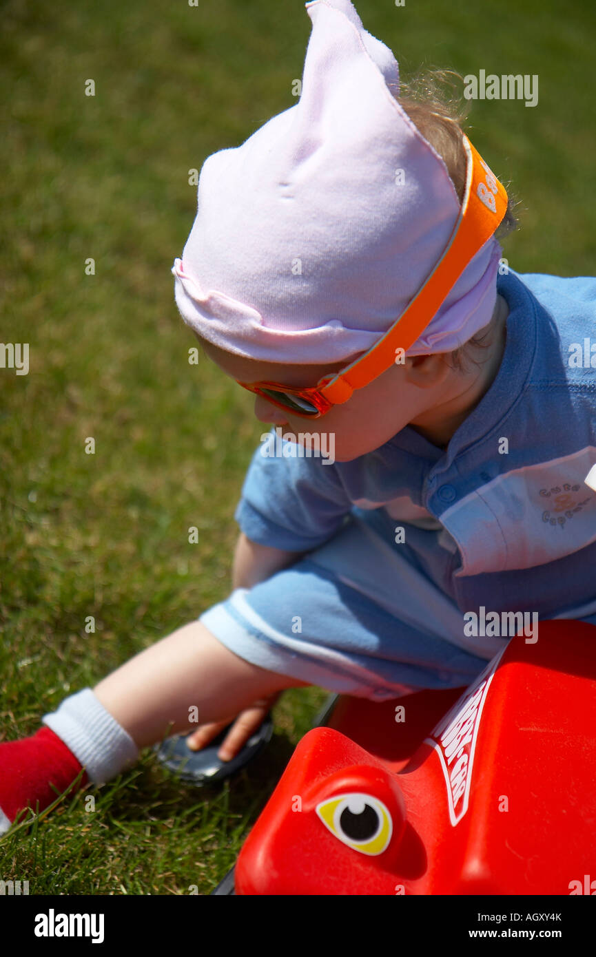 Bébé avec des lunettes de soleil et voiture en plastique rouge Banque D'Images