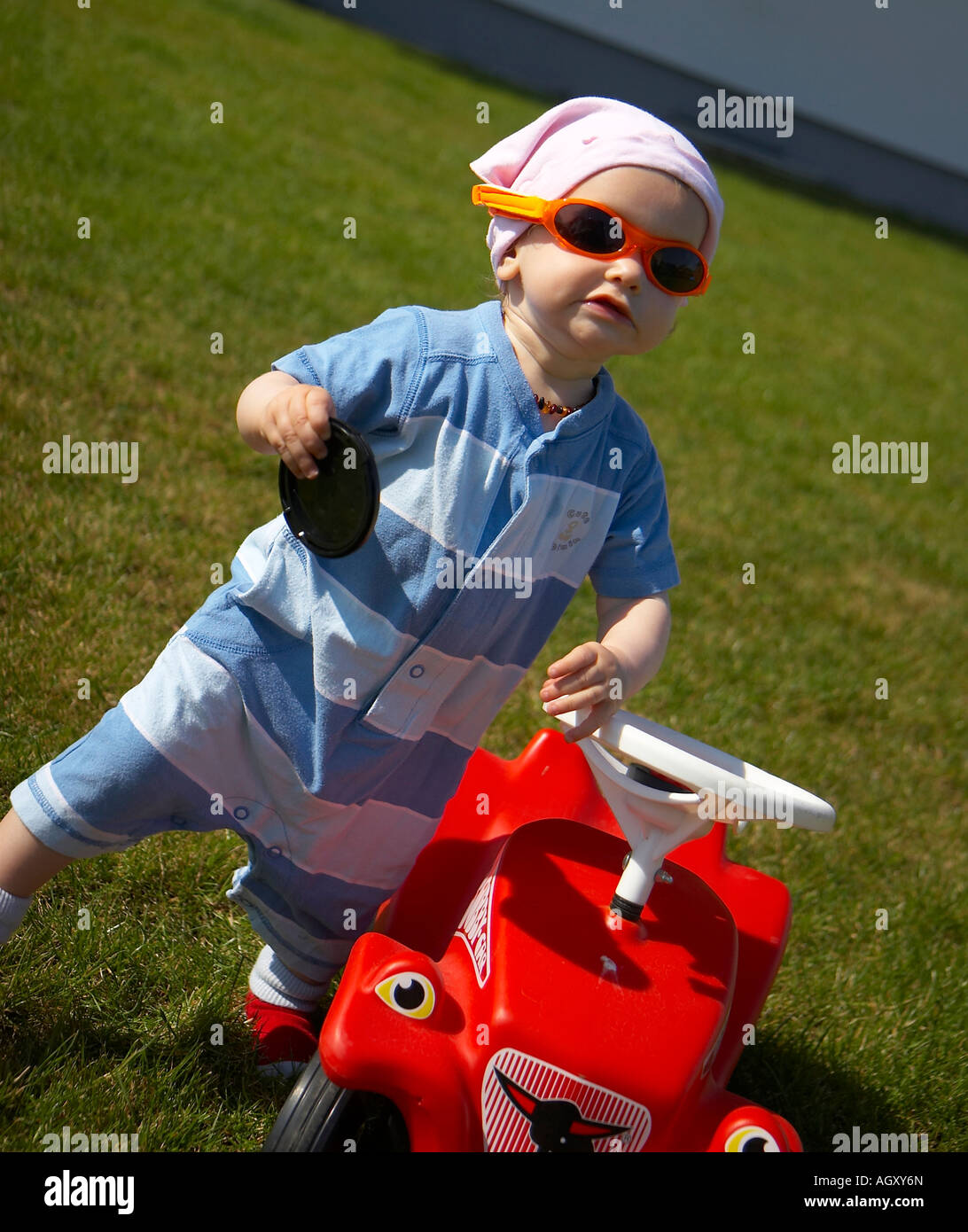 Bébé avec des lunettes de soleil et voiture en plastique rouge Banque D'Images