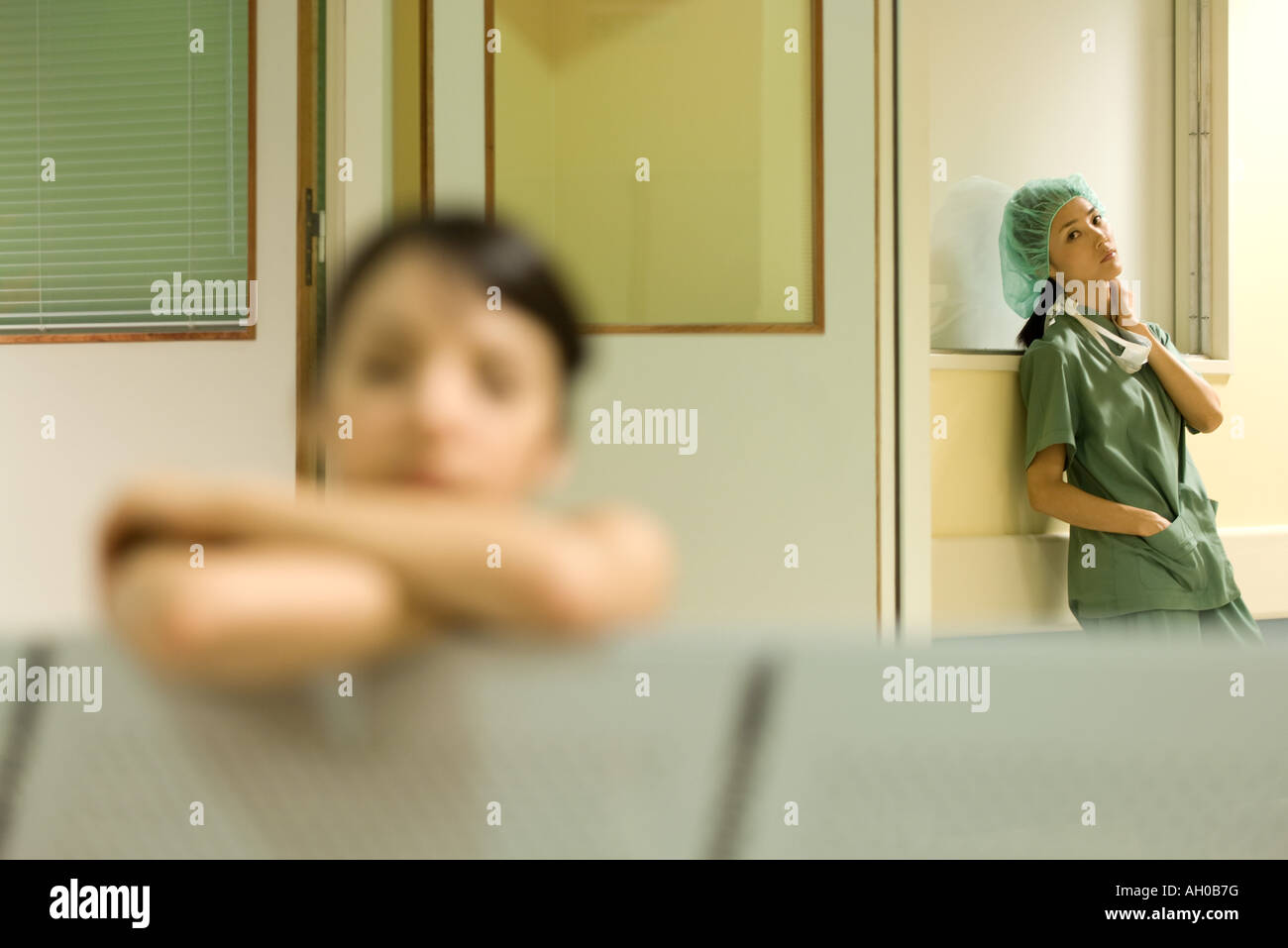 Comité permanent de la santé de l'hôpital en salle d'attente, les mains dans les poches, looking at camera, woman resting head on arms en premier plan Banque D'Images