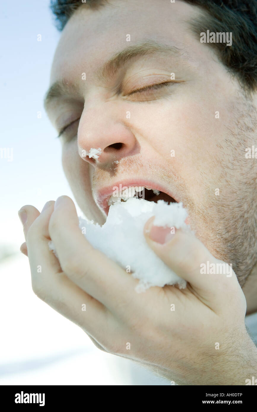 Jeune homme mangeant de la neige, les yeux clos, close-up Banque D'Images
