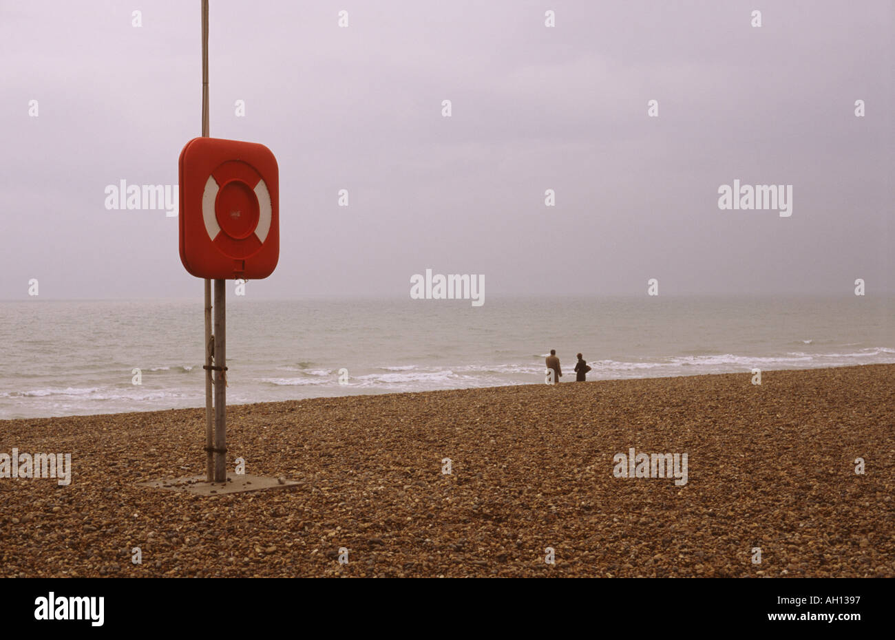 Homme et femme se rencontraient au bord de l'eau sur une plage déserte avec bouée de sauvetage à l'état Prêt. Banque D'Images
