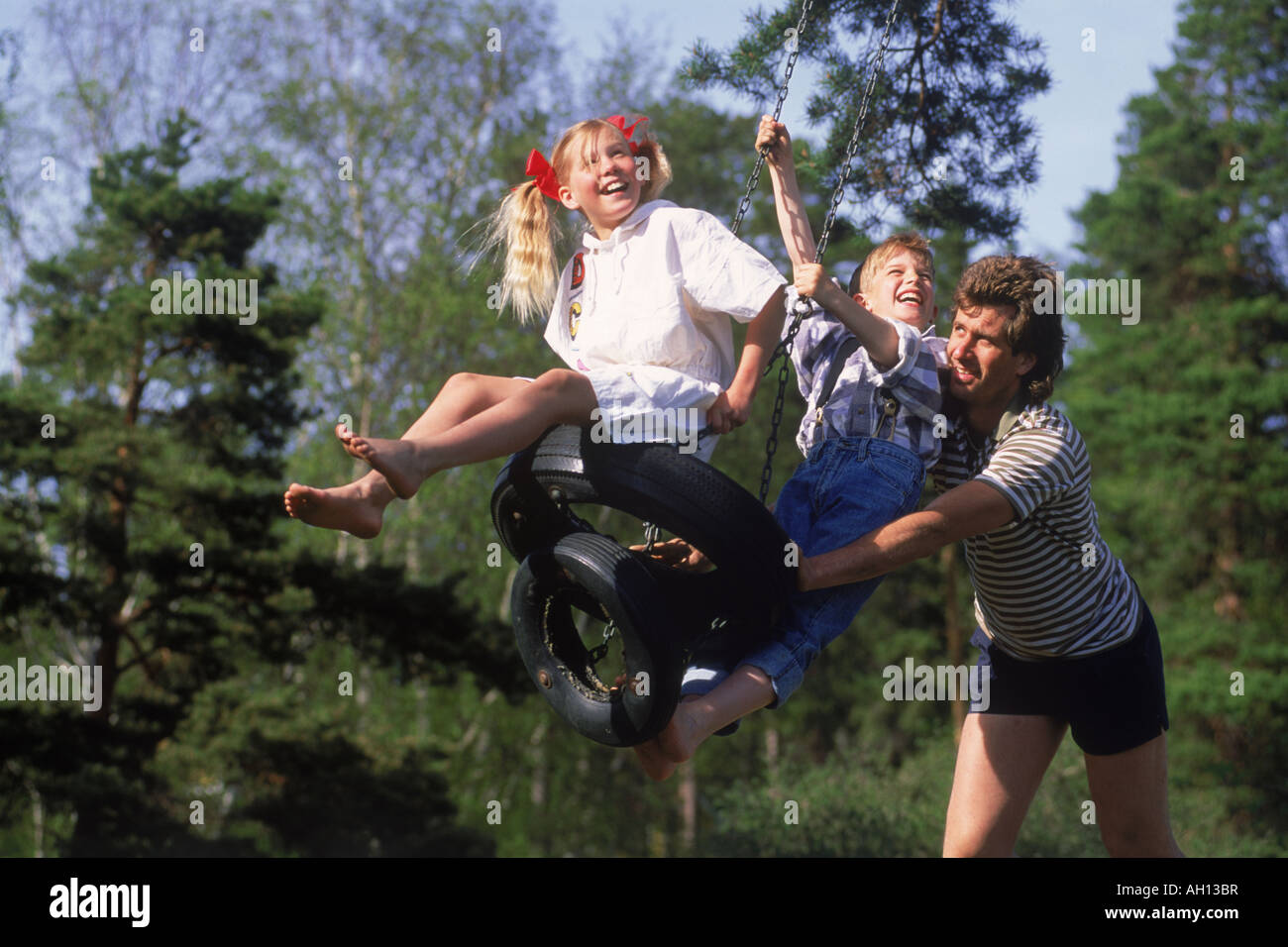 Père aider pousser son and daughter holding swing sur journée d'été en Suède Banque D'Images
