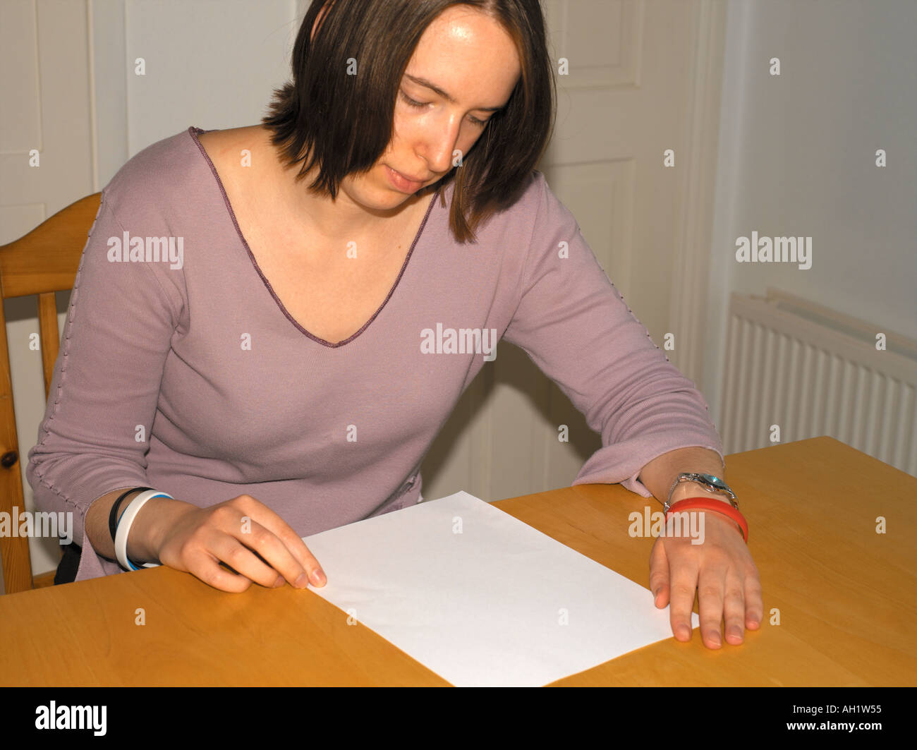Femme regardant une feuille de papier vierge assise à table de cuisine en Angleterre Banque D'Images
