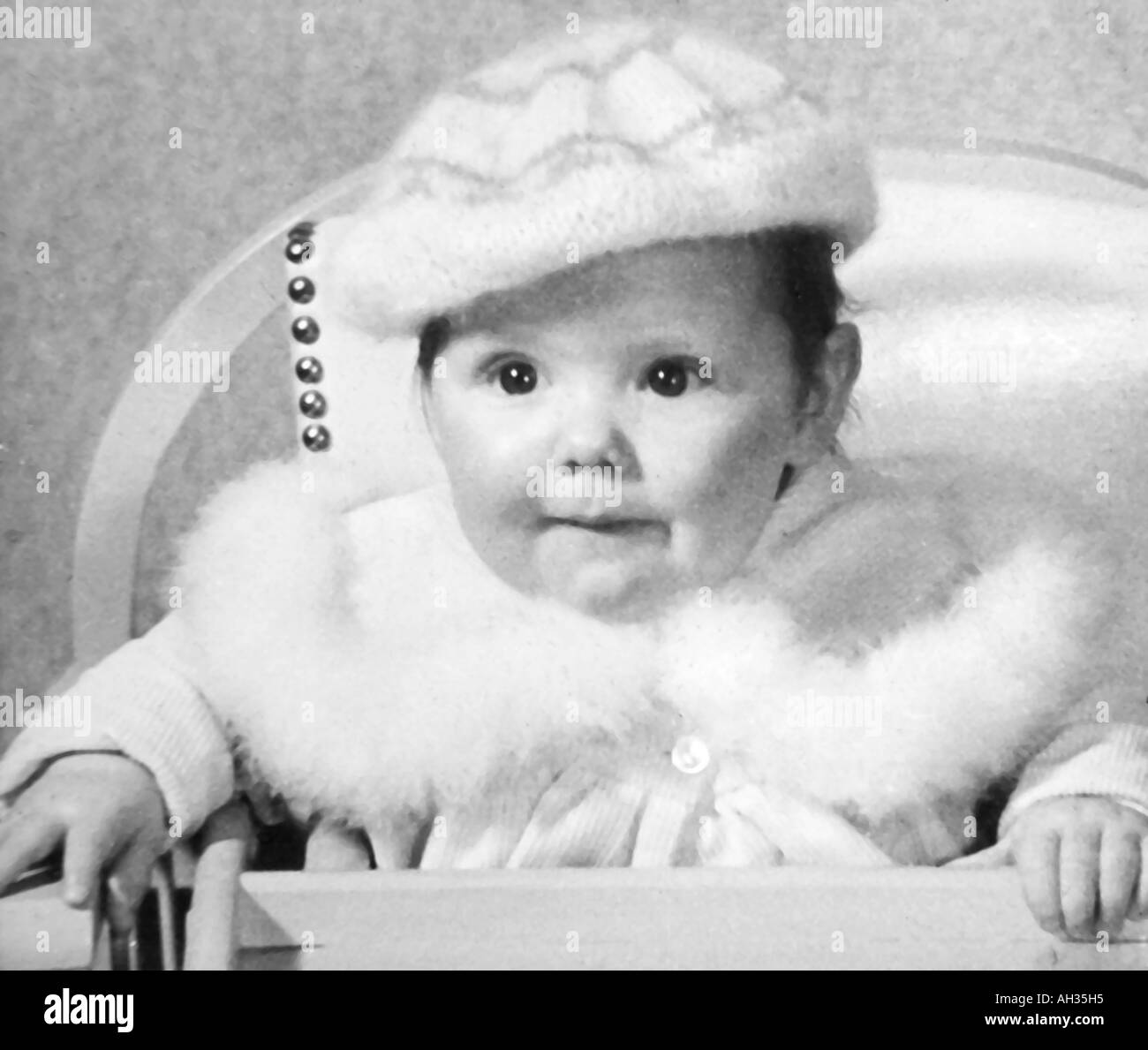 OLD VINTAGE SNAPSHOT FAMILLE PHOTOGRAPHIE DE BABY GIRL WEARING FUR COAT PARÉS ET BONNET DE LAINE assis dans une chaise haute Banque D'Images