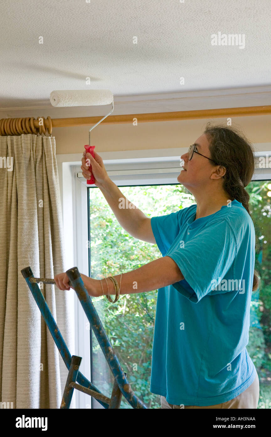 Femme à l'aide d'un rouleau pour peindre un plafond dans une maison d'habitation à Cardiff Wales UK Banque D'Images