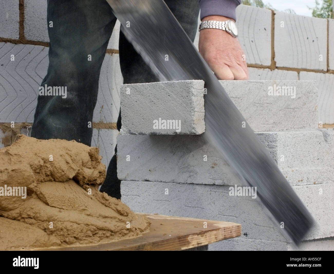 Maçon de flou à l'aide de scie à main pour couper des blocs d'isolation pour mur creux de nouvelle maison avec du sable et du ciment mélange de mortier sur mortier bord England UK Banque D'Images