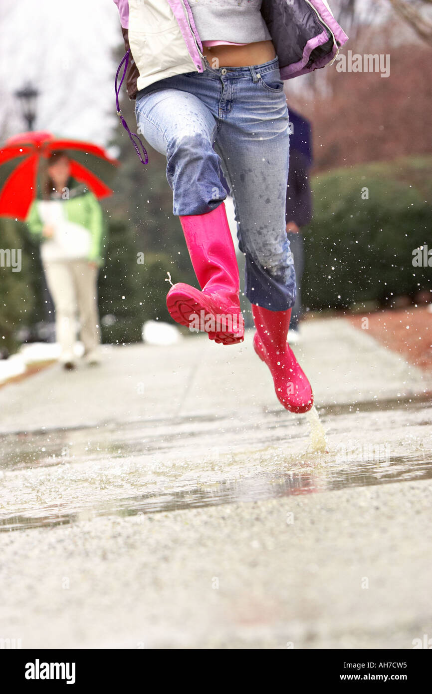 Jeune femme sauter dans une flaque d'eau avec des amis en arrière-plan l'exercice parapluies dans la pluie 12 29 ans 20 ans 20 s 20 30 Banque D'Images