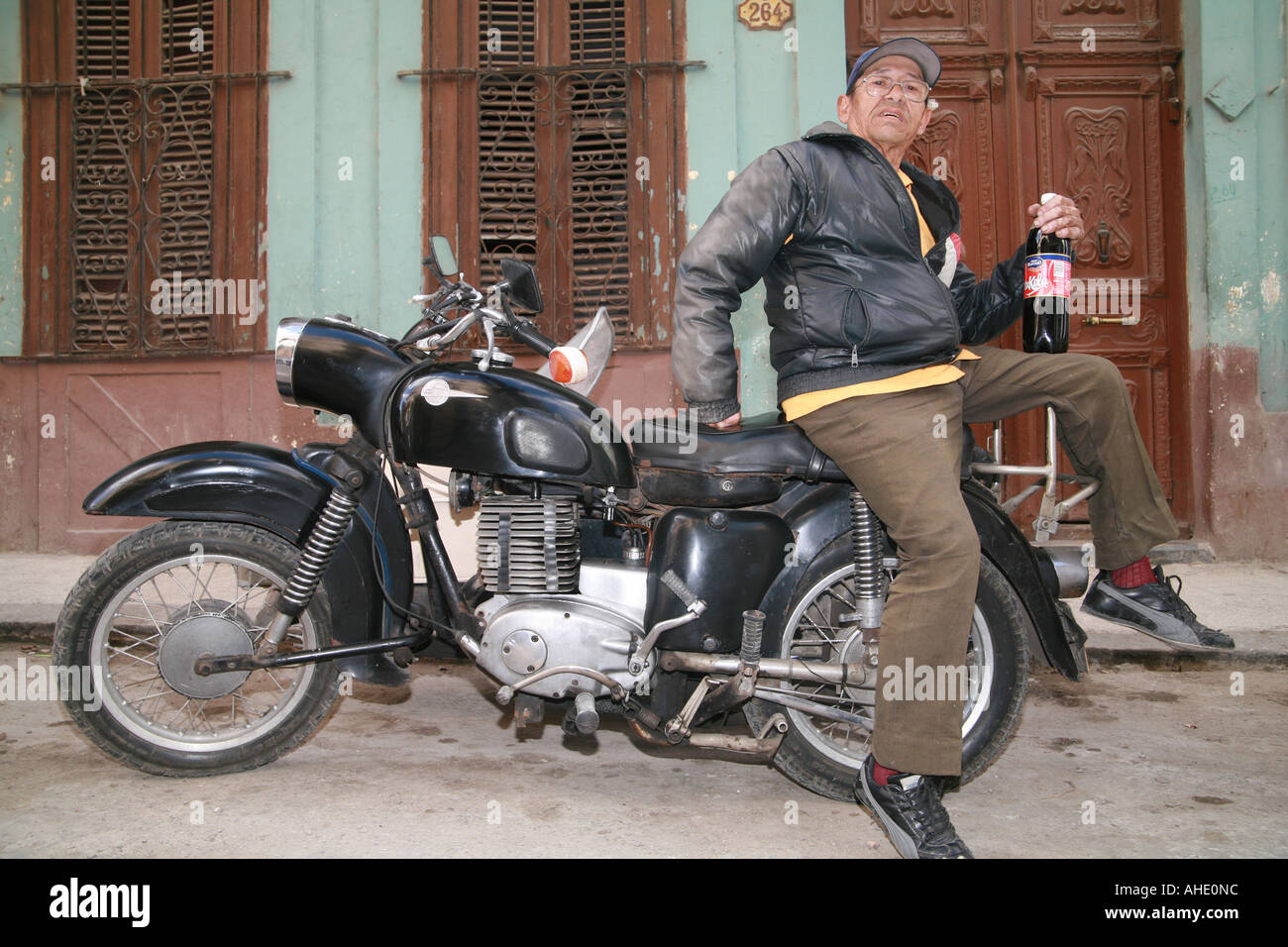 Cuba La Havane un homme âgé sur sa moto vintage tenant une bouteille avec Coke Cola tu national Banque D'Images