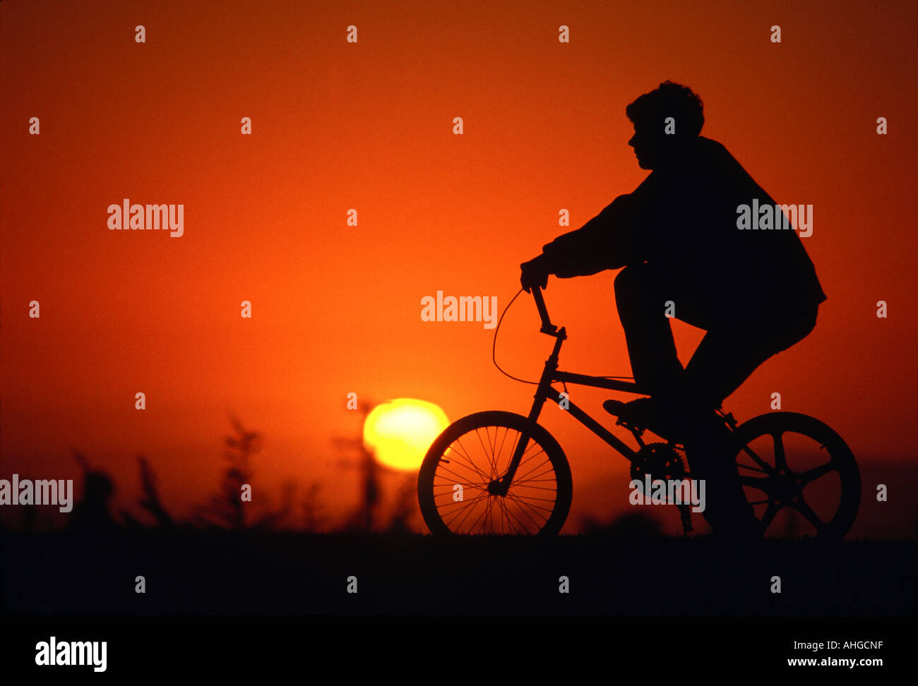 La silhouette d'un garçon et vélo avec fond coucher de soleil rouge Banque D'Images