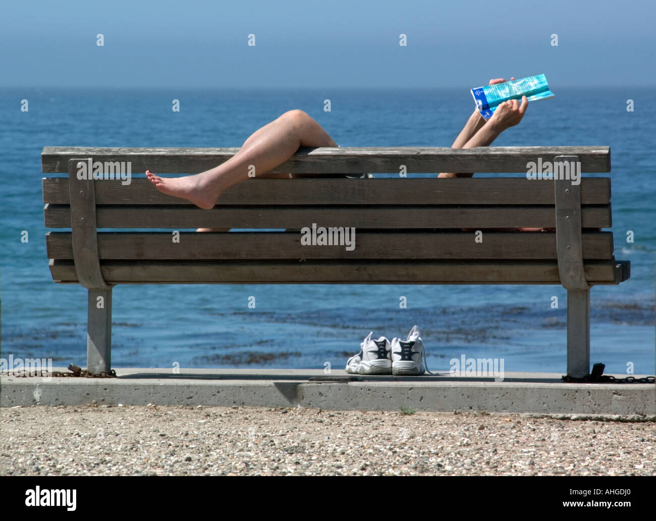 Une femme lit un livre dans une position délicate sur un banc avec vue sur l'océan. Banque D'Images