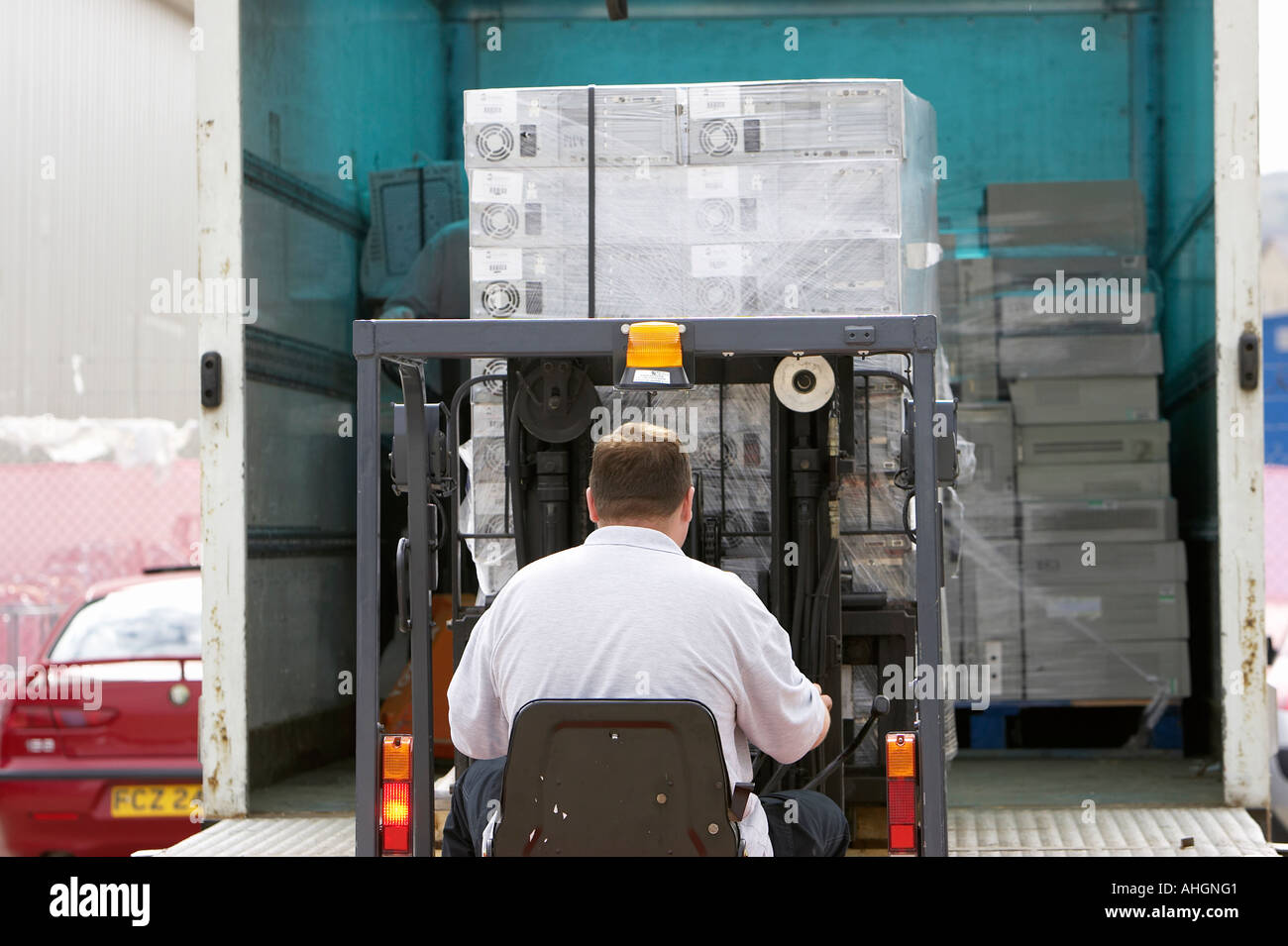 Ouvriers déchargement camion avec plateau élévateur chariot contenant palette enveloppée des piles de boîtes de système informatique Banque D'Images