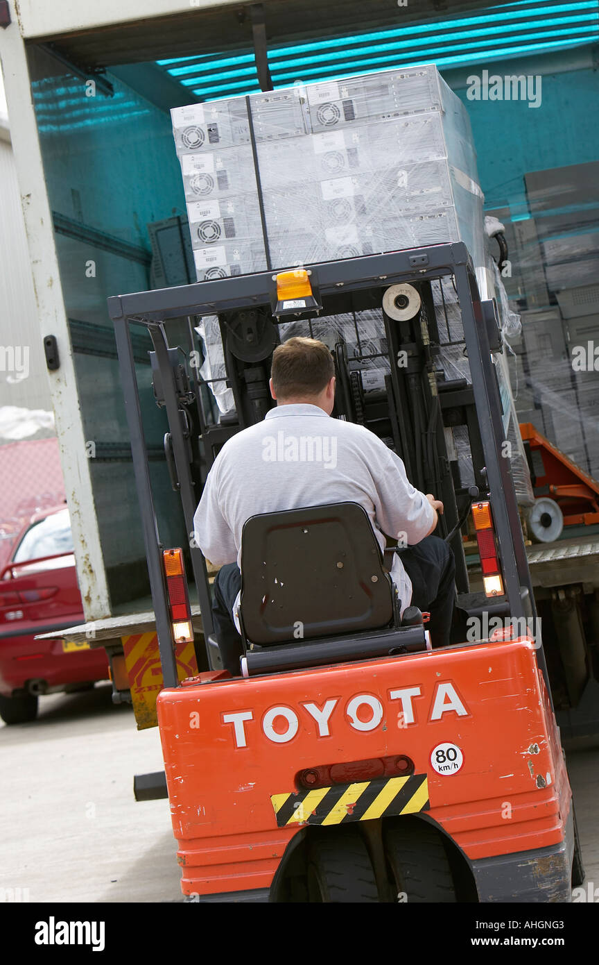 Ouvriers déchargement camion avec plateau élévateur chariot contenant palette enveloppée des piles de boîtes de système informatique Banque D'Images