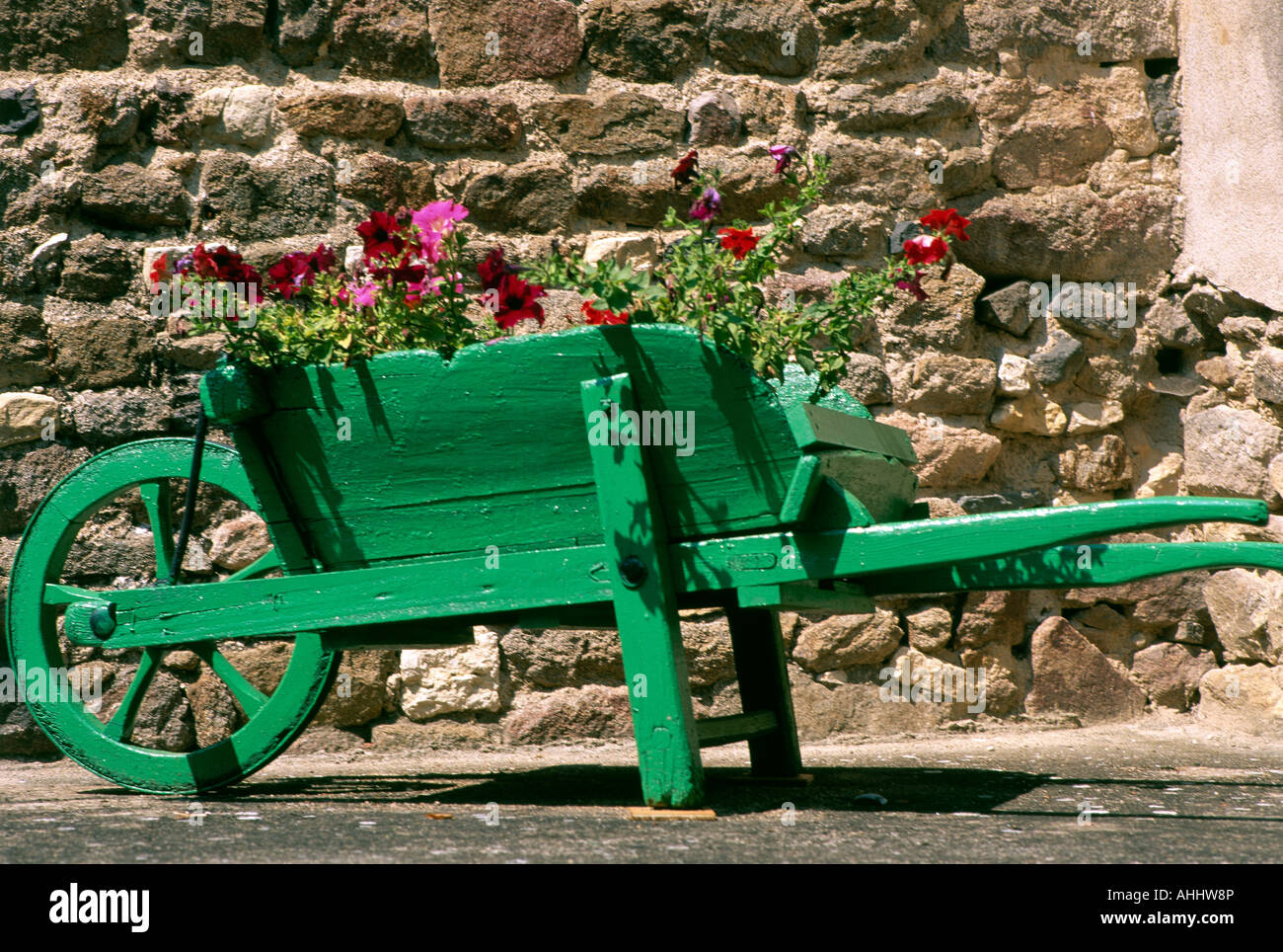 Une brouette en bois vert rempli de fleurs colorées et situé à côté d'un mur de pierre brute dans le petit village de Sai Banque D'Images