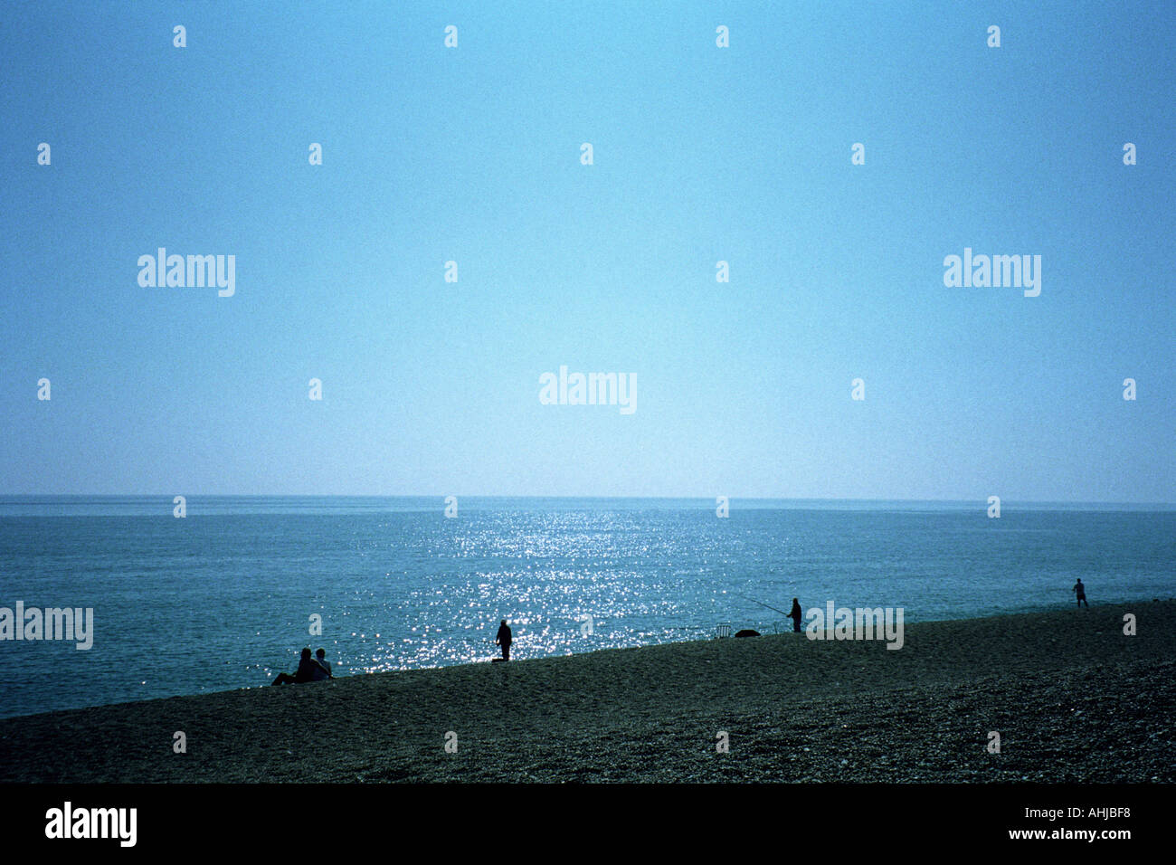 Vue sur la mer depuis Chesil Beach avec la lumière du soleil sur l'eau. Pêcheurs et un couple silhoueté sur le rivage. Chesil Beach, Dorset, Royaume-Uni. Banque D'Images