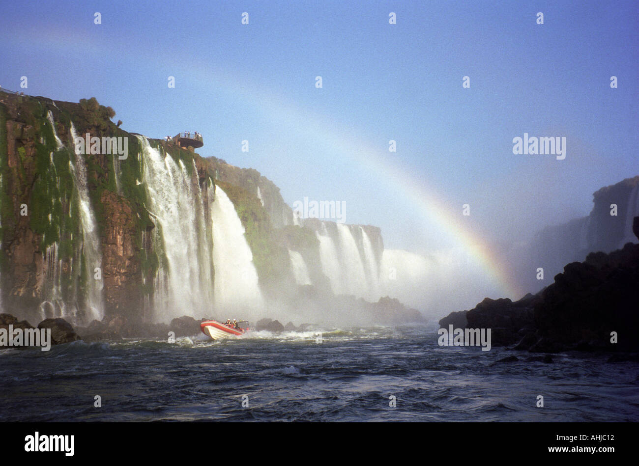 Bateau d'excursion avec côtes rouges et blanches à l'entrée de la section de la gorge du Devils des chutes d'Iguaçu avec arc-en-ciel et plate-forme d'observation au-dessus. Etat de Parana, Brésil. Banque D'Images