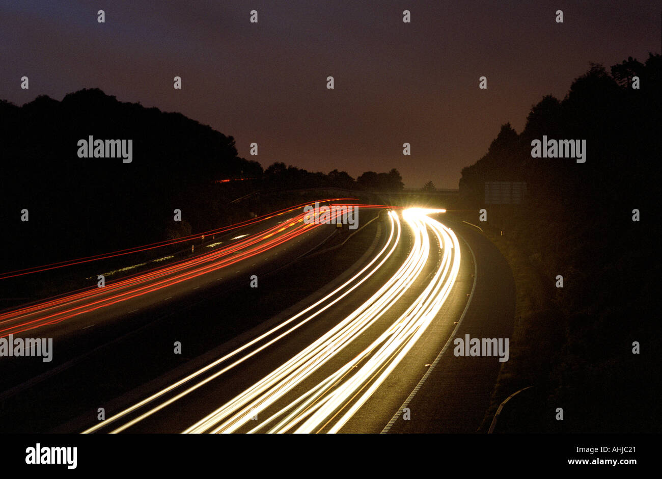 Traînées de feux de voiture blancs et rouges sur l'autoroute M3 avec des arbres silhouettés contre le ciel. Twyford Cutting, Hampshire, Royaume-Uni. Banque D'Images