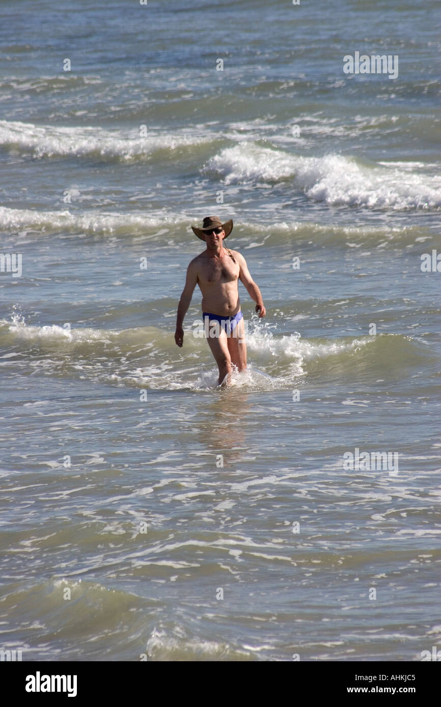 Man Wearing Hat et Swimtrunks Walking in Surf plage de Glenelg Adelaide Australie Banque D'Images