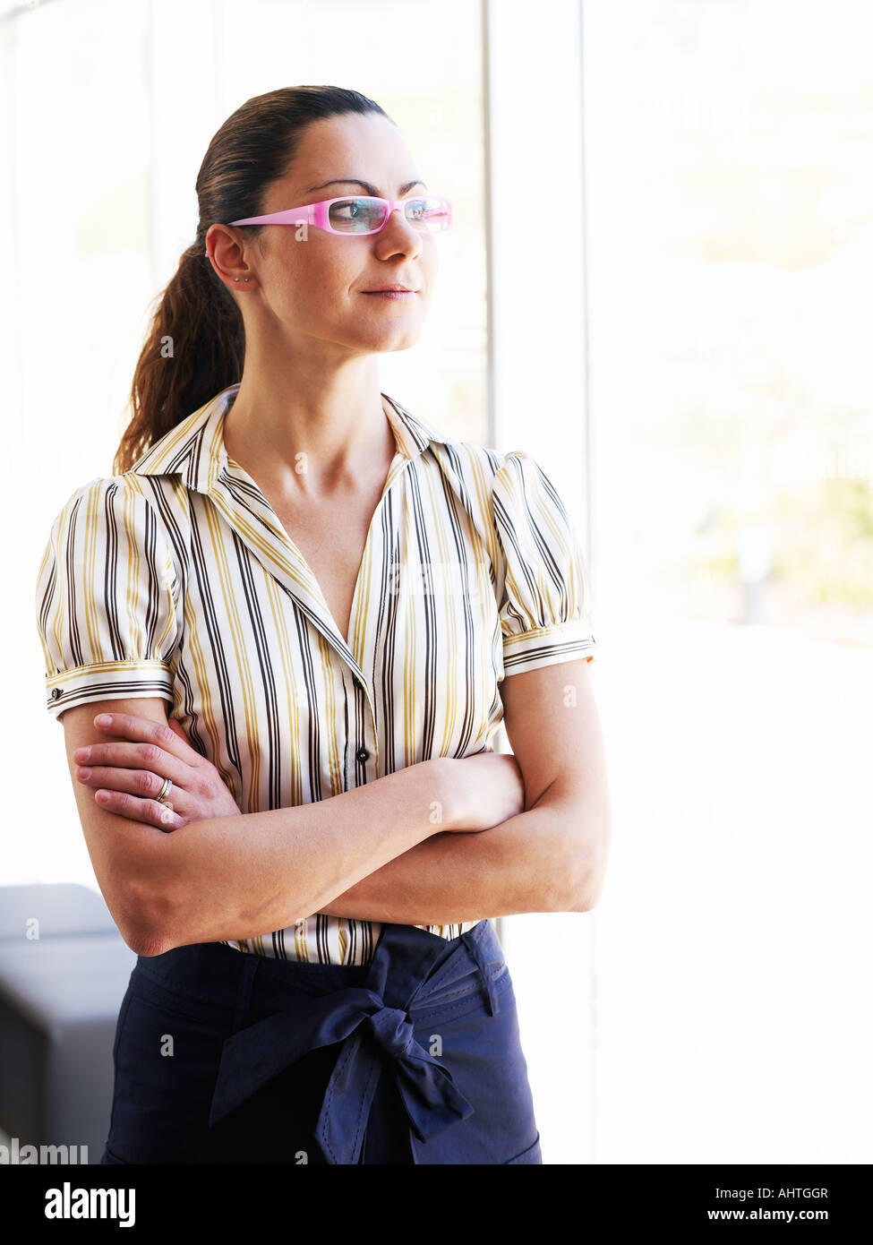 Businesswoman standing par fenêtre, les bras croisés Banque D'Images