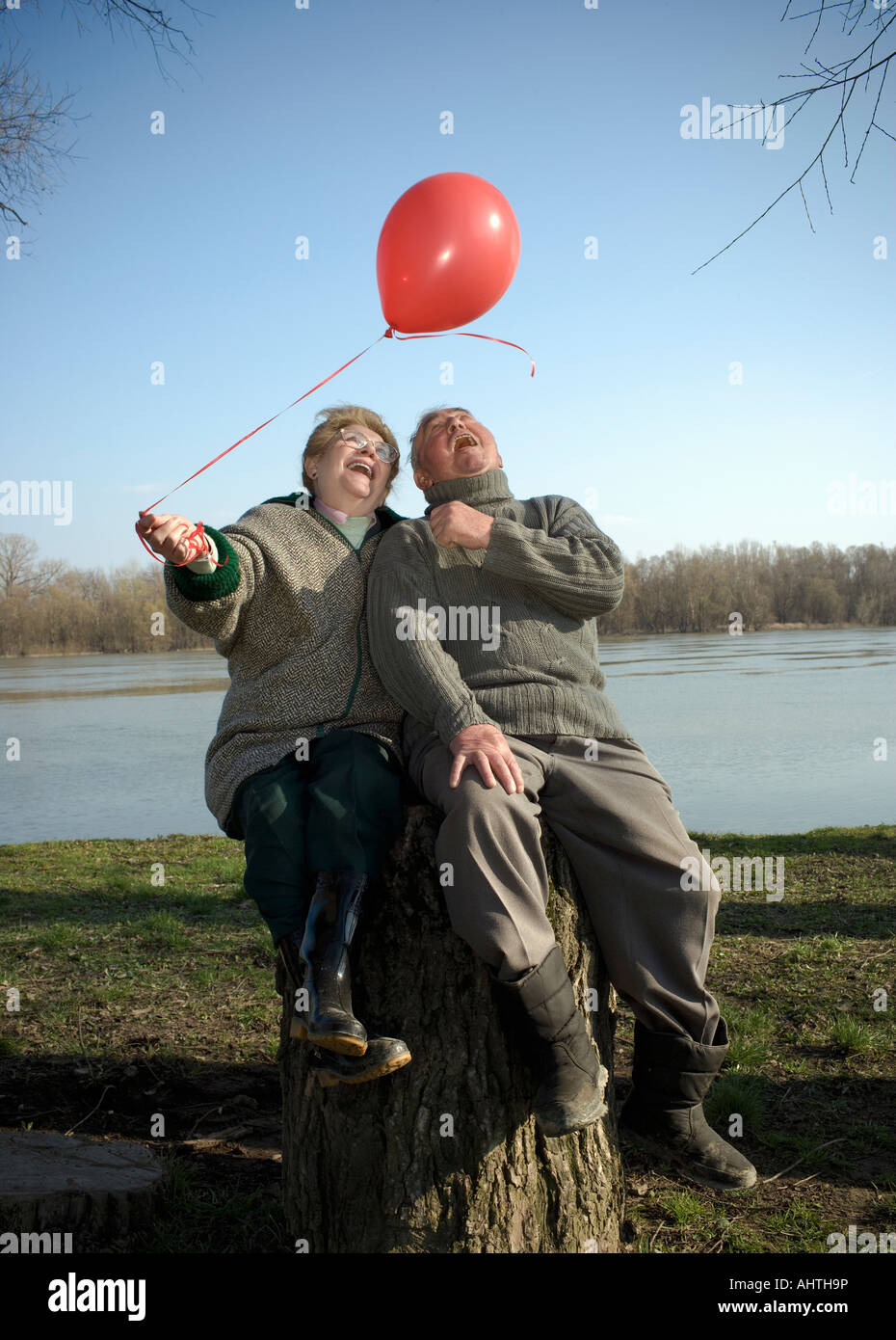 Senior couple sitting by river holding red balloon, smiling Banque D'Images
