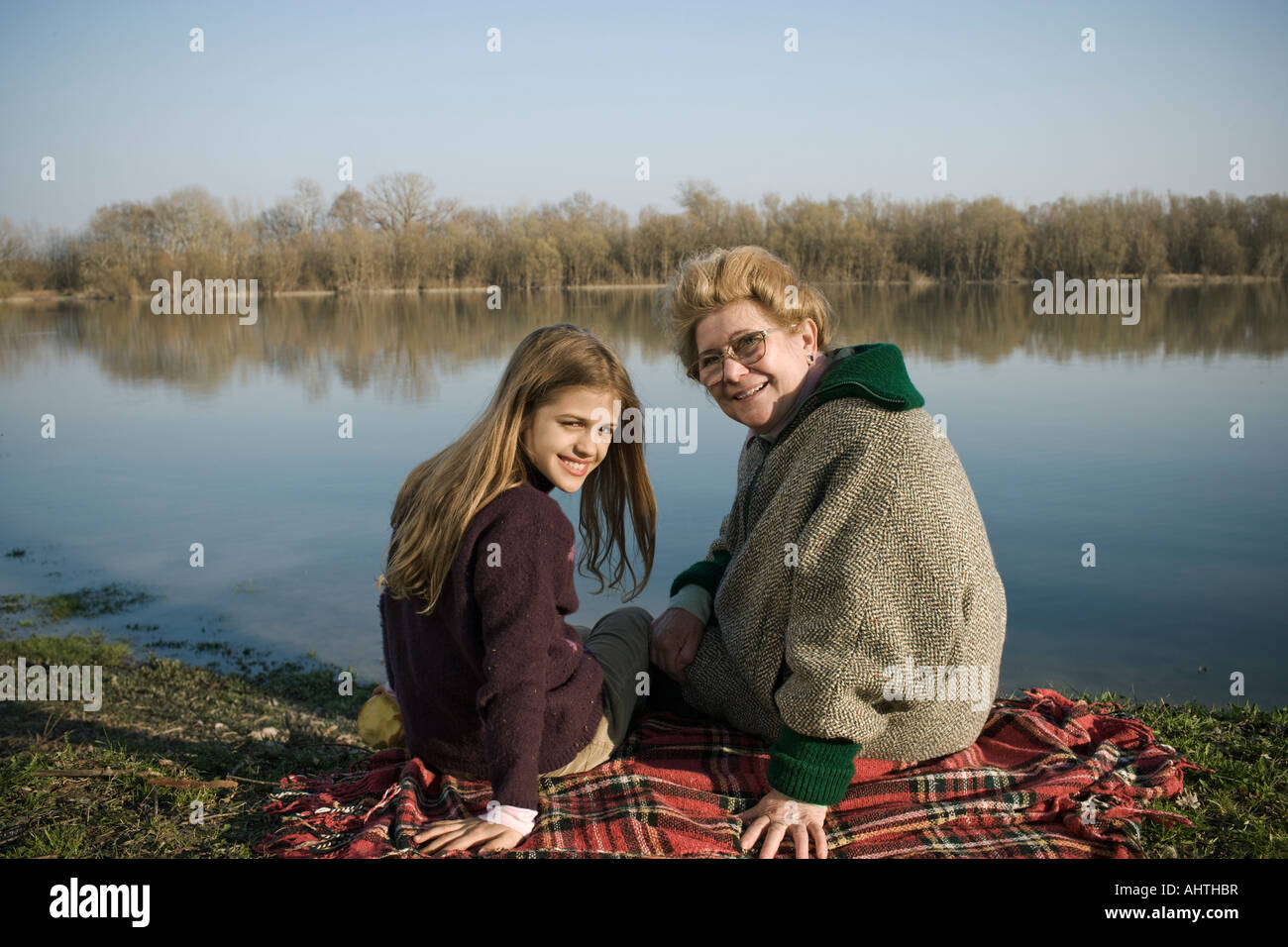 Grand-mère et petite-fille (10-12) assis sur un tapis par rivière, smiling Banque D'Images