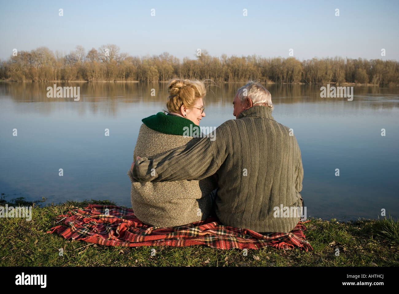 Senior couple sitting on rug par rivière, vue arrière, woman smiling Banque D'Images