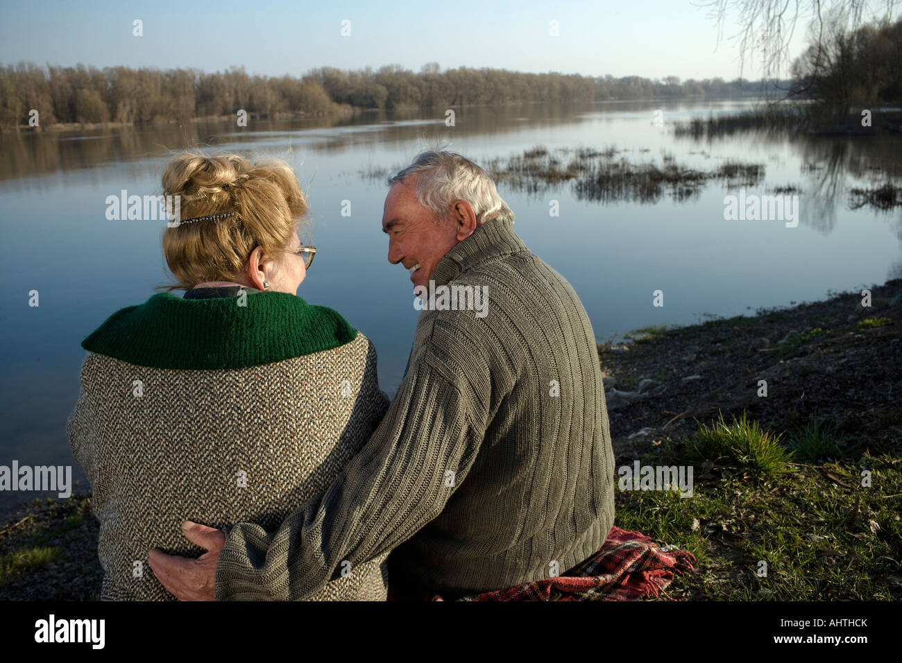 Senior couple sitting on rug par rivière, vue arrière, man smiling Banque D'Images