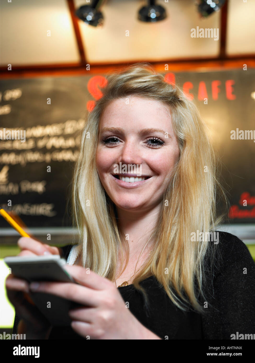 Young waitress holding notepad dans cafe, smiling, portrait Banque D'Images