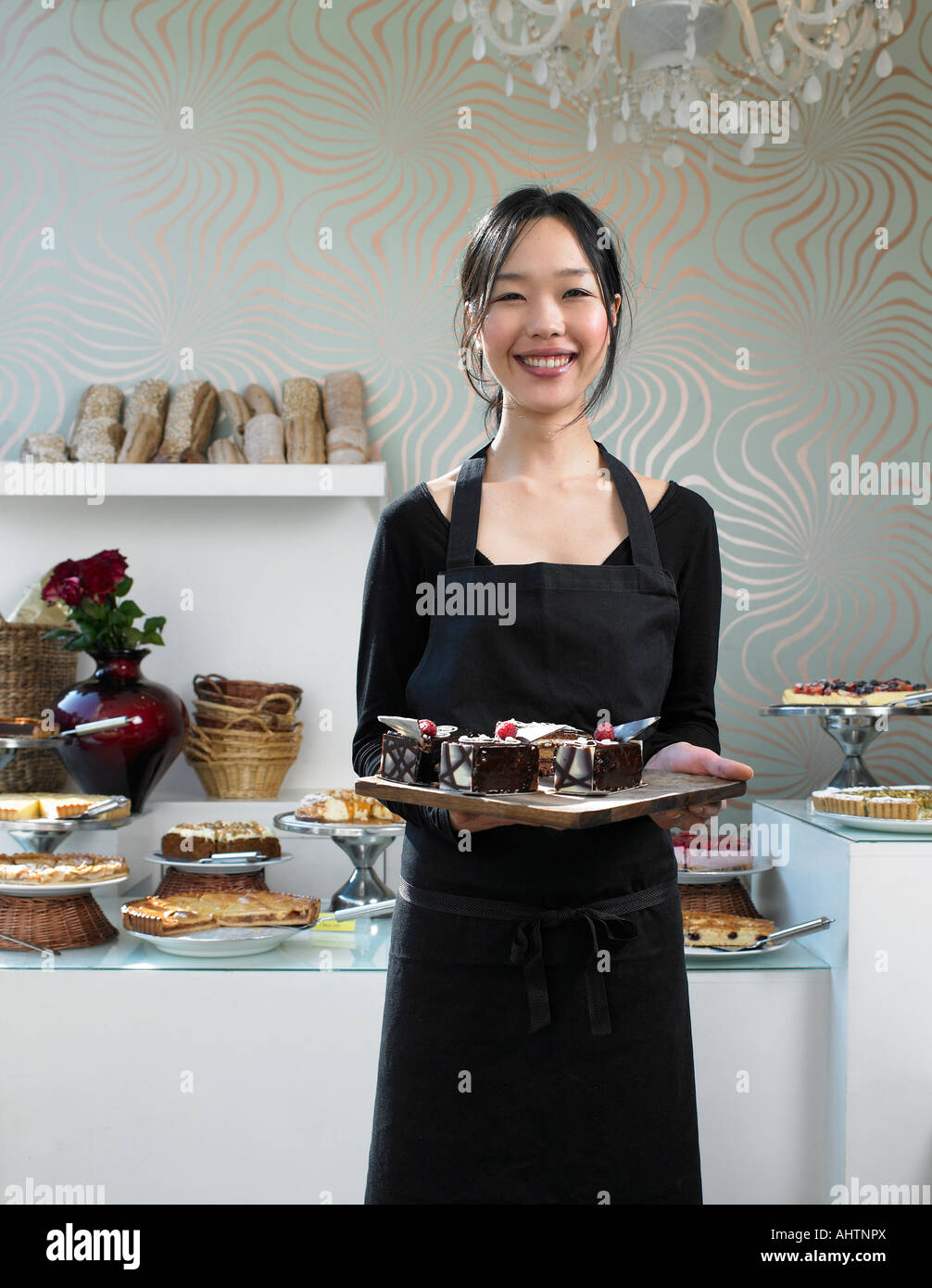 Young waitress holding tray of desserts, smiling, portrait Banque D'Images
