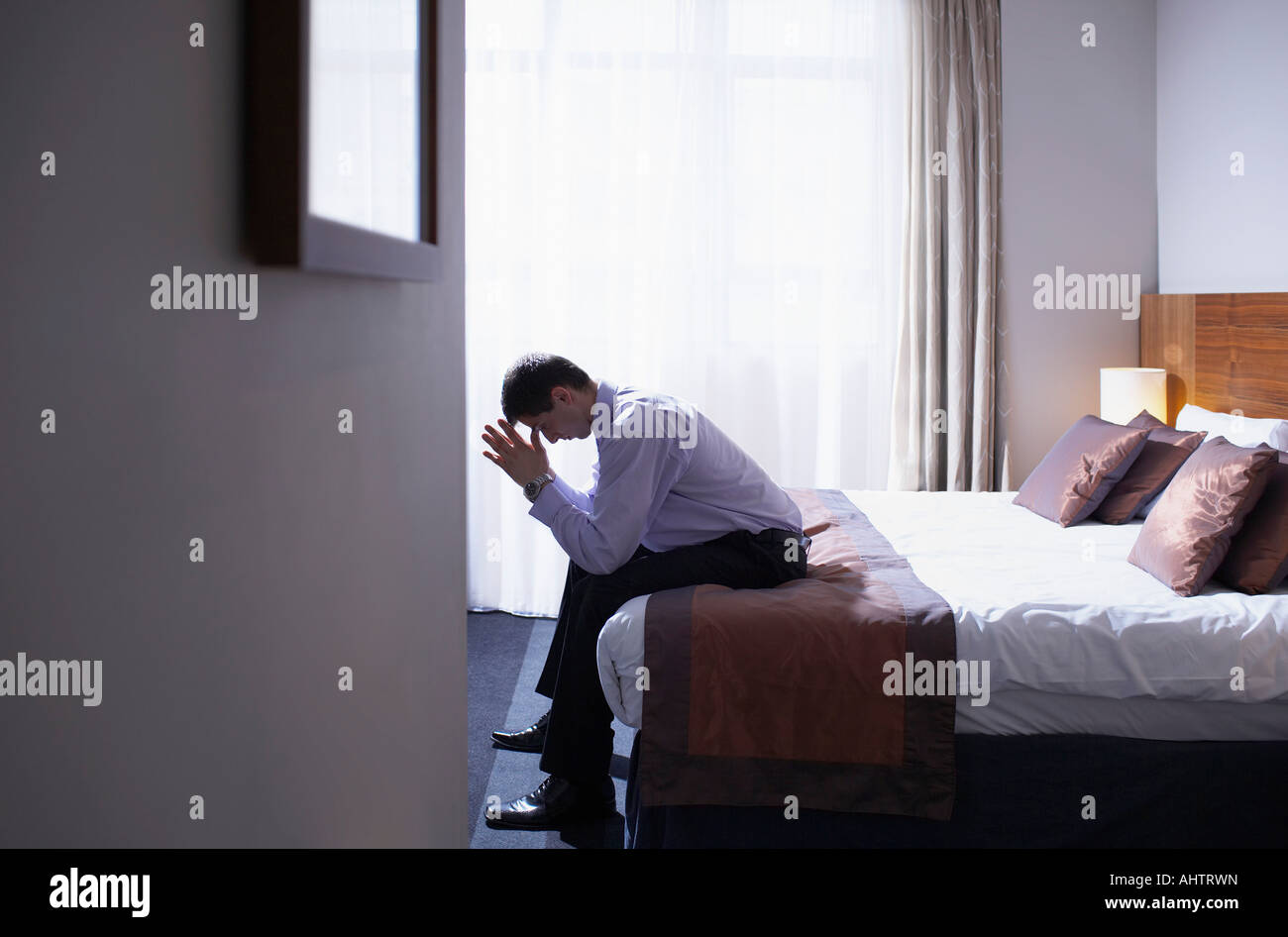 Homme assis sur le bord du lit avec la tête dans les mains Photo Stock -  Alamy