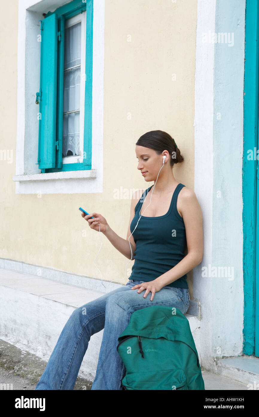 Jeune femme assise à l'extérieur de maison grecque avec sac à dos et  d'écouteurs à MP3 à afficher Photo Stock - Alamy