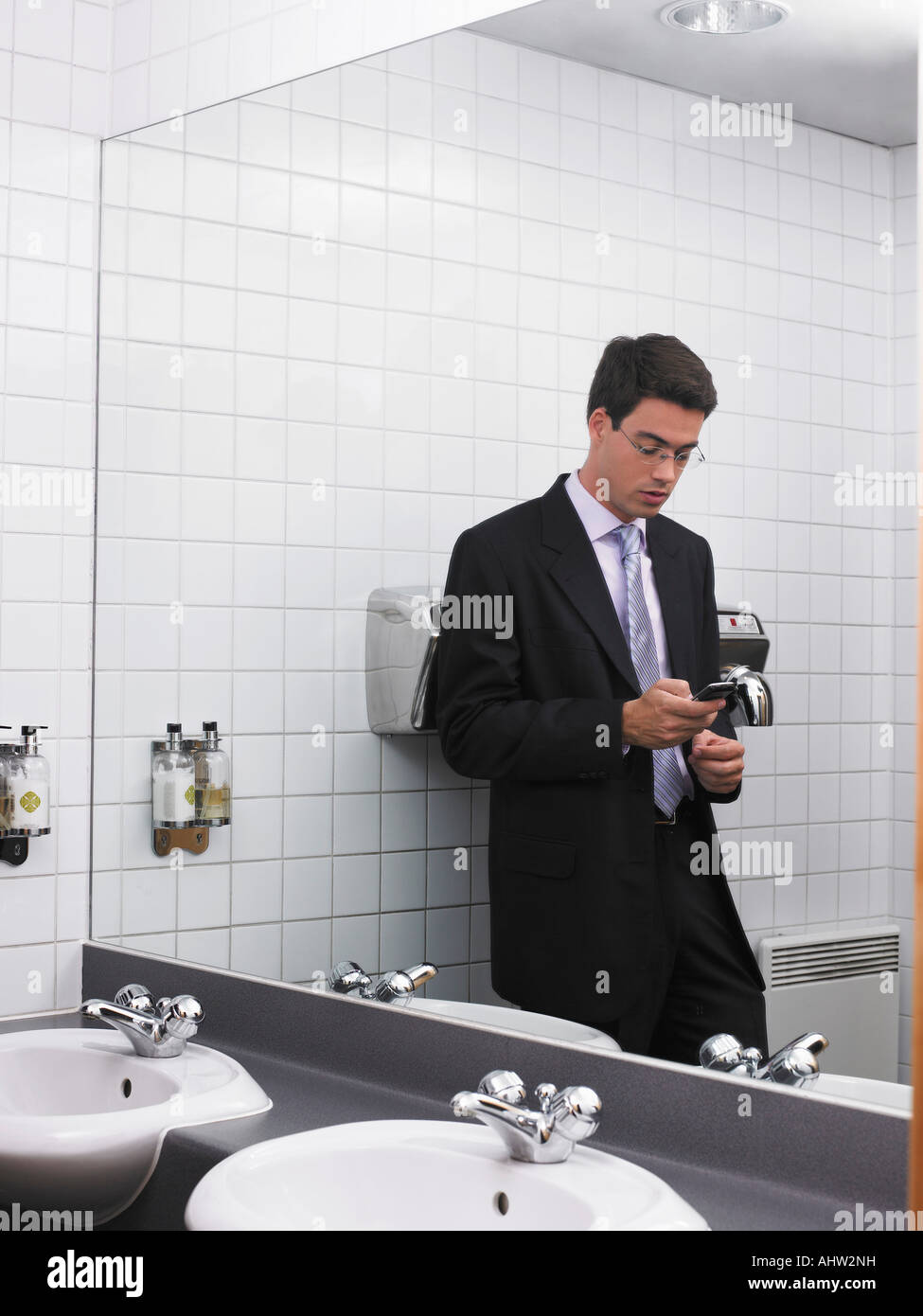 Bureau de l'homme reflétée dans un miroir de toilette à l'aide de mobile phone Banque D'Images