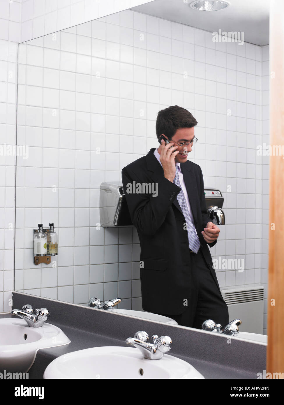 Bureau de l'homme reflétée dans un miroir de toilette à l'aide de mobile phone Banque D'Images