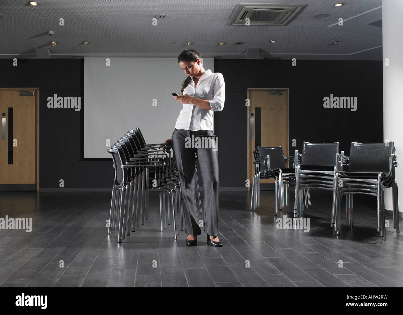 Femme debout avec pile de chaises en salle de présentation vide Banque D'Images