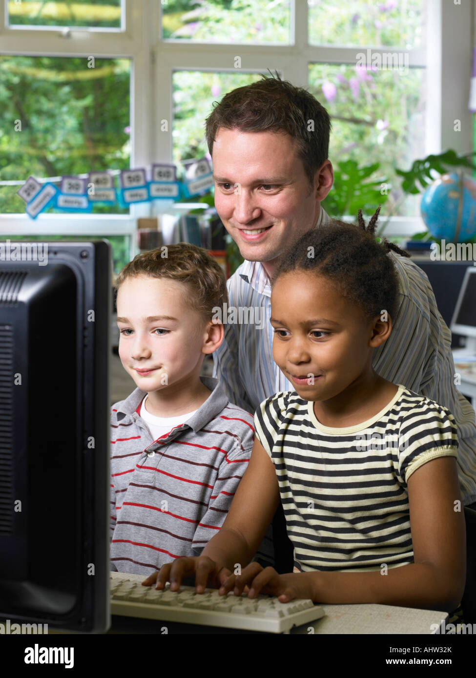 Enseignant de sexe masculin à la recherche à l'écran d'ordinateur avec garçon et fille Banque D'Images