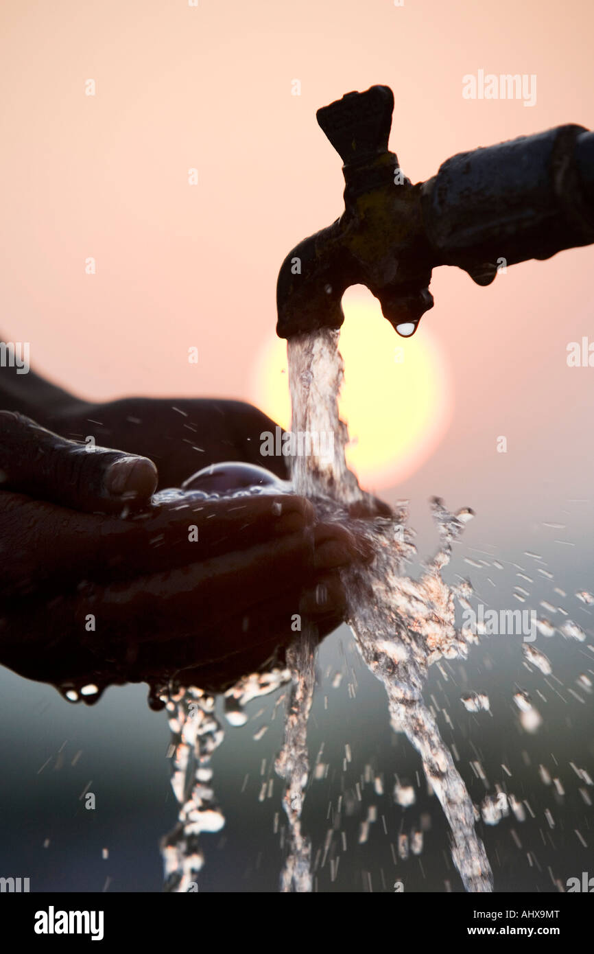 La collecte de l'eau au creux des mains d'un robinet de tuyau au lever du soleil. L'Inde. Silhouette Banque D'Images