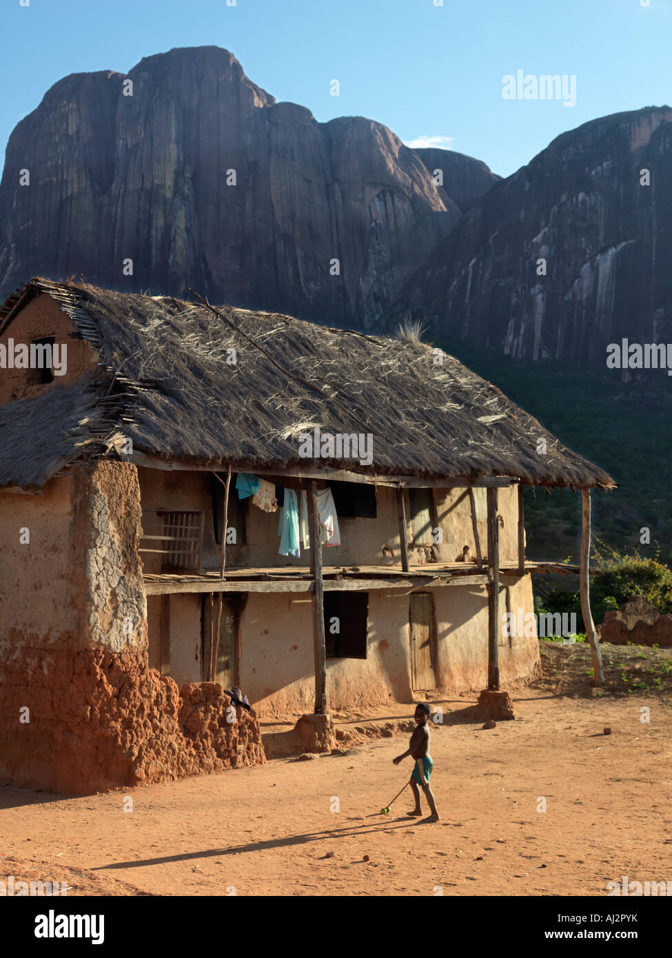 Un jeune garçon malgache joue avec son jouet fait maison à l'extérieur de sa maison, une maison à étages double Betsileo Banque D'Images