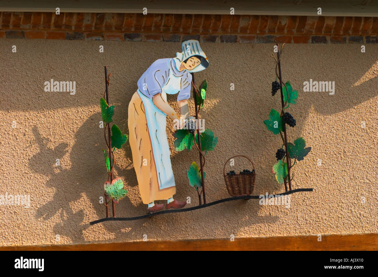 Une enseigne peinte en fer forgé qui illustre le thème de la production de vin et champagne : une femme en vêtements traditionnels pour la récolte des raisins, la vigne et un panier de raisins, le village d'Hautvillers dans la vallée de la Marne, Champagne, Marne, Ardennes, France Banque D'Images