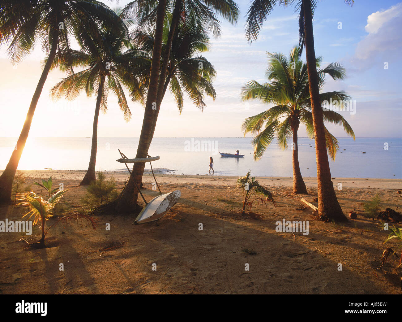 Woman walking along sandy shore au coucher du soleil avec pirogue sur l'île d'Aitutaki aux Îles Cook Banque D'Images