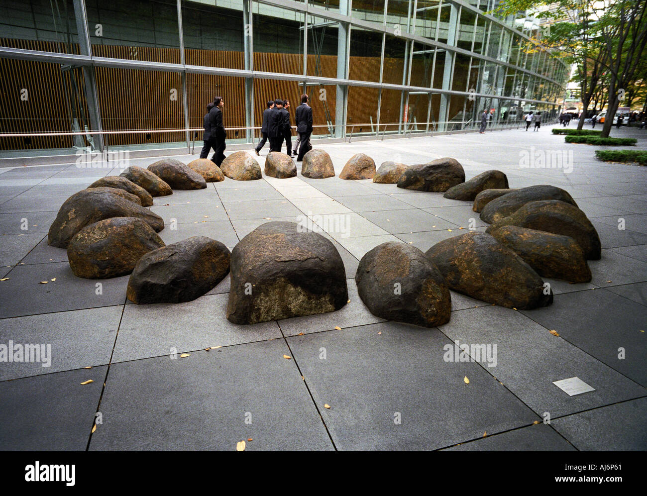 Un groupe d'hommes sur pause déjeuner passe par un cercle de pierres dans le cadre d'une exposition d'art permanente en dehors de la Tokyo International Forum Banque D'Images