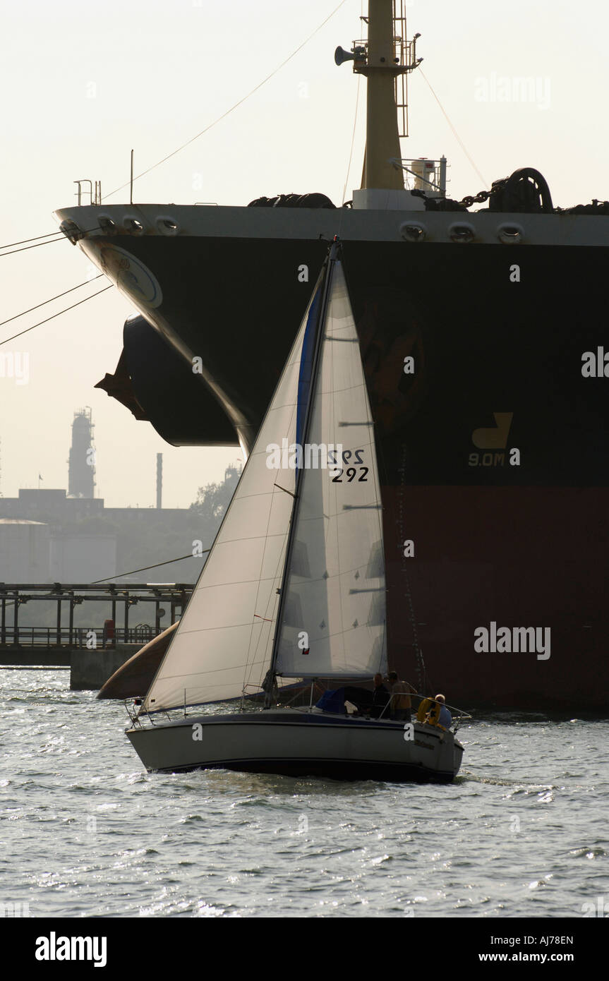 Un petit cruising yacht sails passé le pétrolier la liberté comme il l'Olympique se charge dans le Solent, Angleterre Banque D'Images