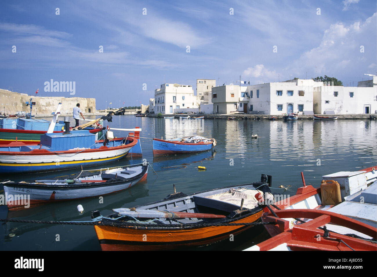 Un homme sur le pont d'un petit bateau de la flotte de pêche amarrés dans le vieux port de bizerte corsair encerclée par les maisons blanches et bleues de la Médina à côté du murs en pierre jaune de la Kasbah Tunisie Banque D'Images