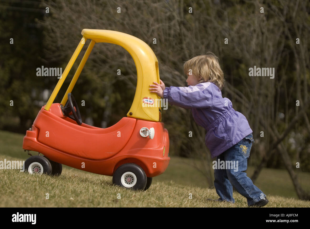 Une petite fille a poussé sa petite voiture dans l'herbe comme lors d'un jour frais de printemps. Banque D'Images