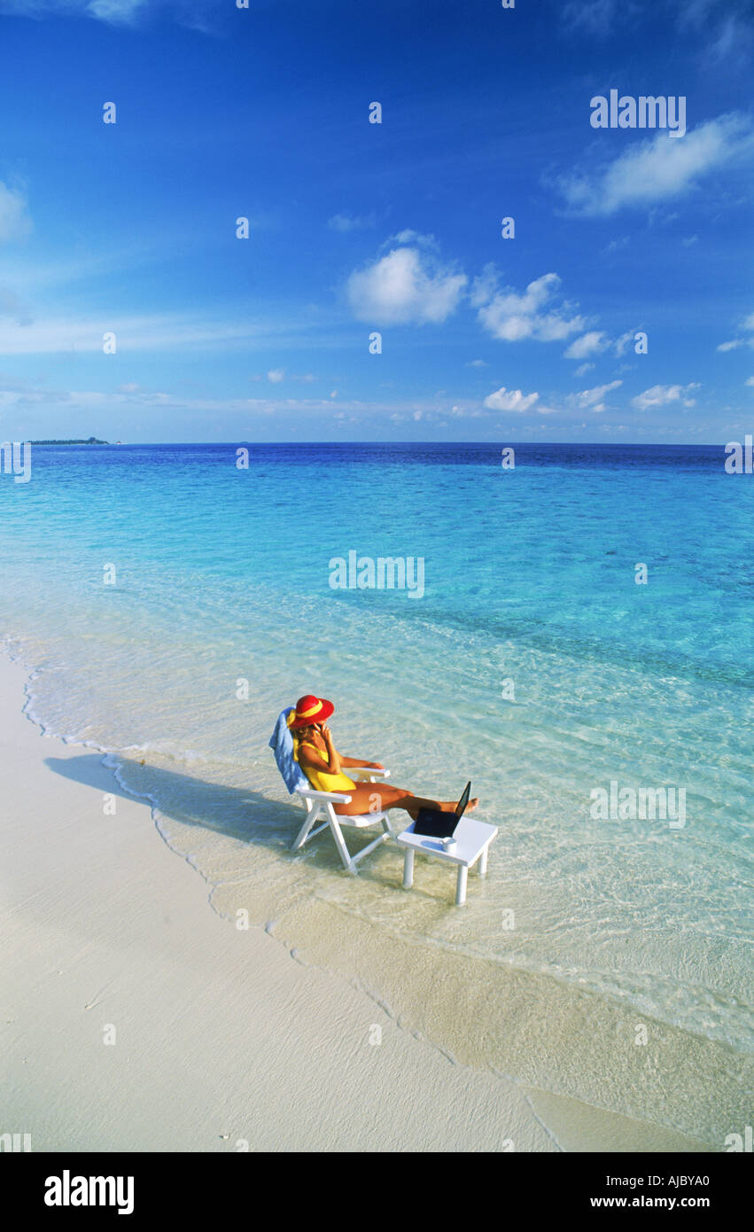 Femme assise à table avec ordinateur portable et téléphone portable sur la plage aux Maldives Banque D'Images