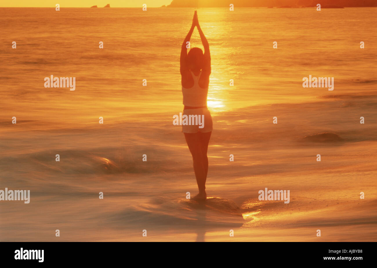 Woman in yoga position silhouetté par le coucher du soleil à Laguna Beach en Californie Banque D'Images